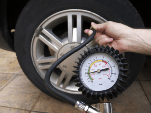 Driver checking tire pressure before a summer road trip to ensure safe driving conditions.