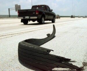 Blown tire on the side of the highway with a black truck driving past.