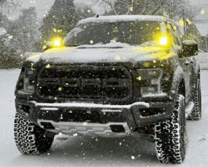 Car with fog lights on, driving through a snowy landscape, showing how fog lights improve visibility.