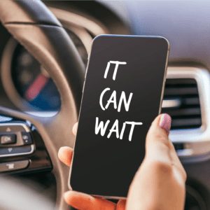 a driver holding a cell phone that says "It can wait"